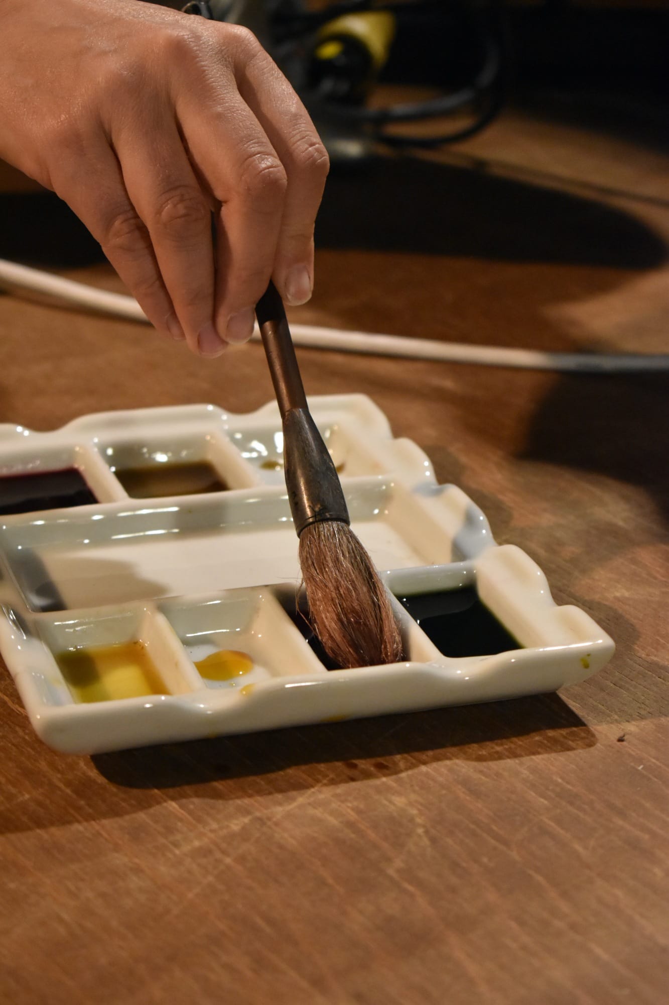 a hand holds a brush dipping into a watercolor well