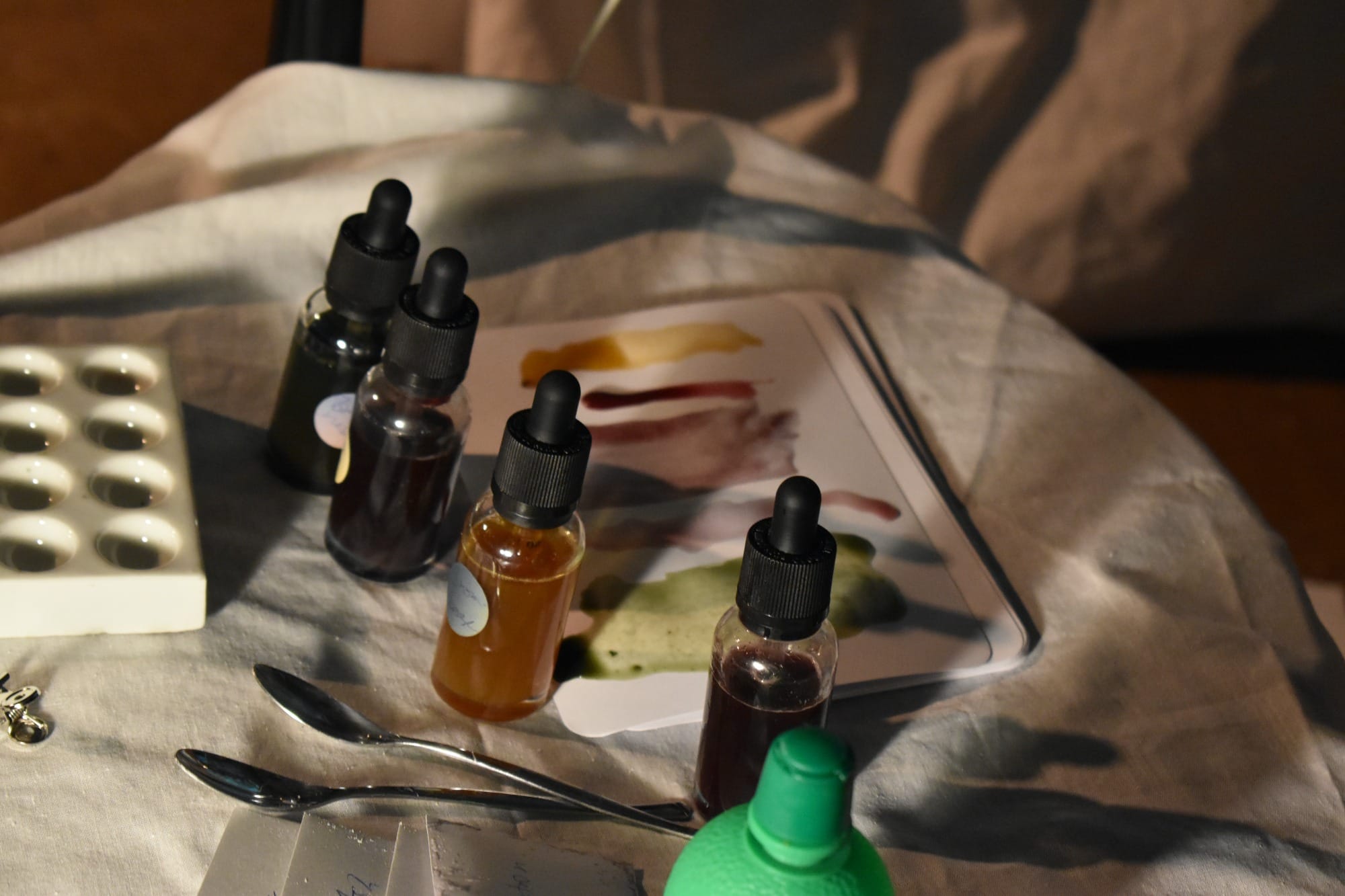 a set of coloured droppers on a table with spoons and paper with colour samples