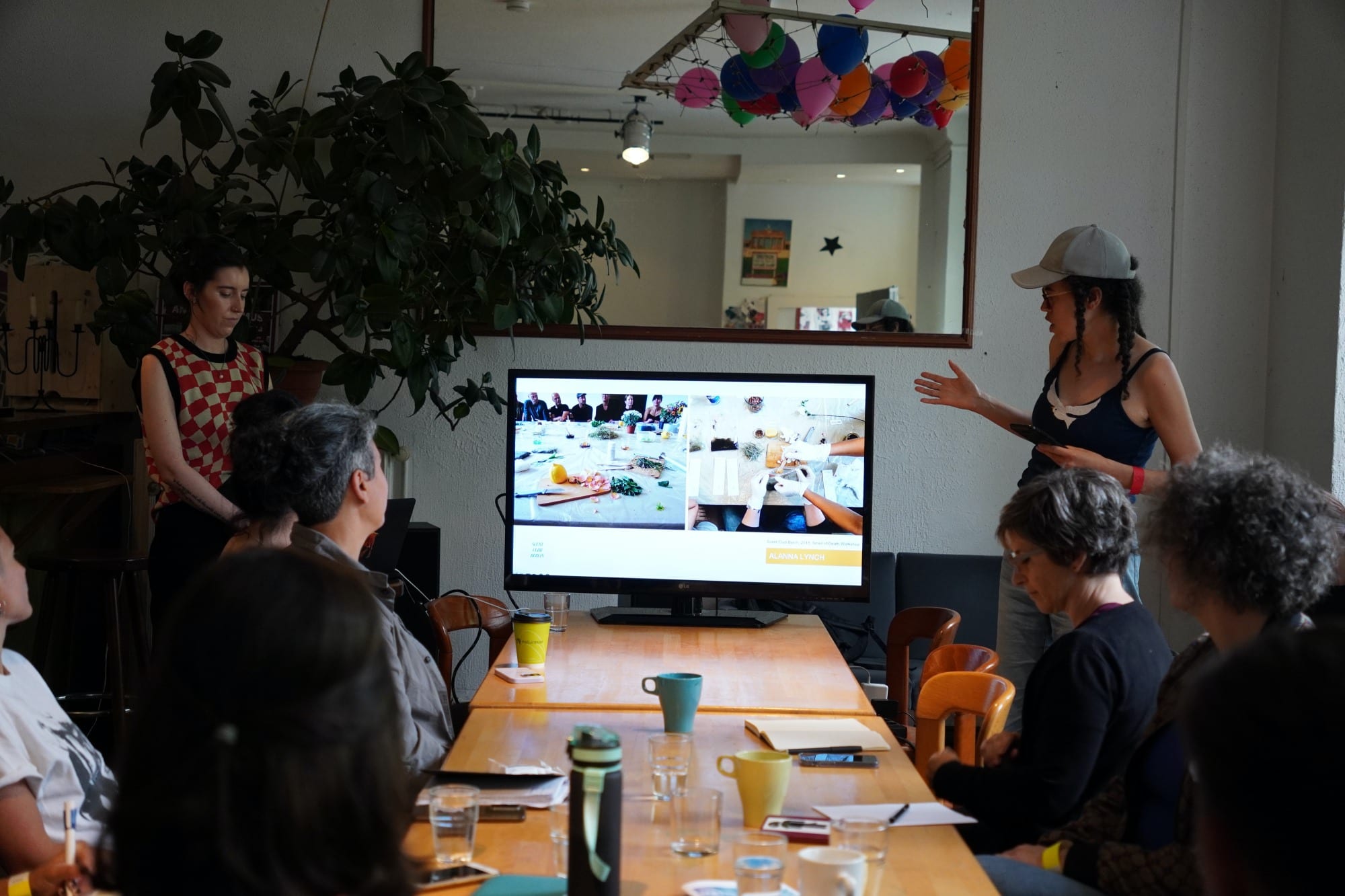 people sitting at a table, two standing, a monitor on the table