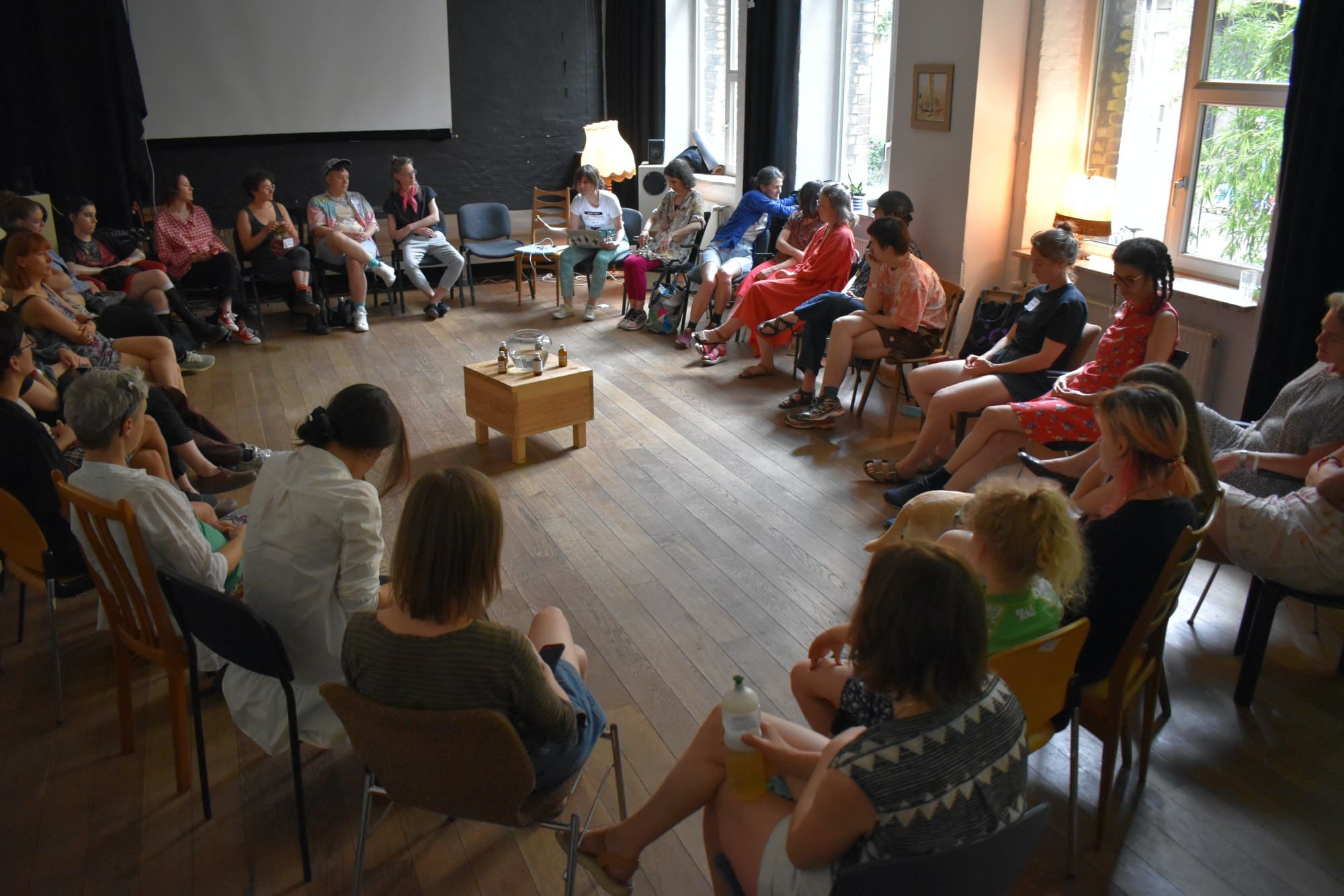 women sitting in a circle a table with a large glass vessel in the center
