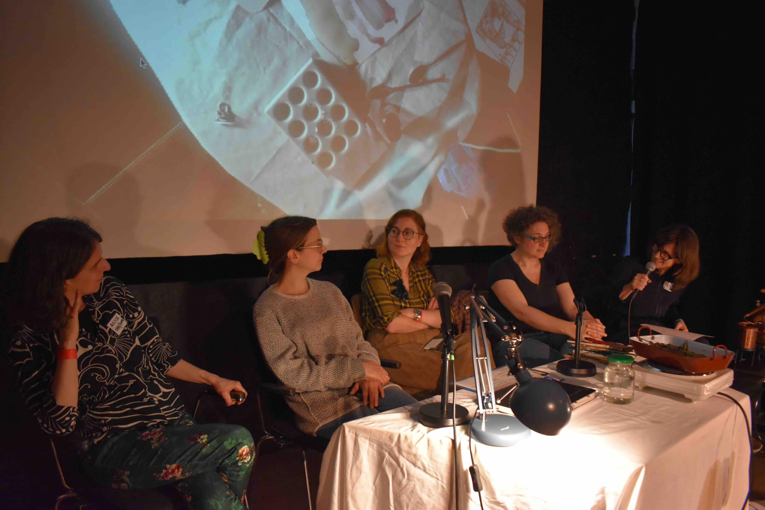five women seated at a podium a projection in the background