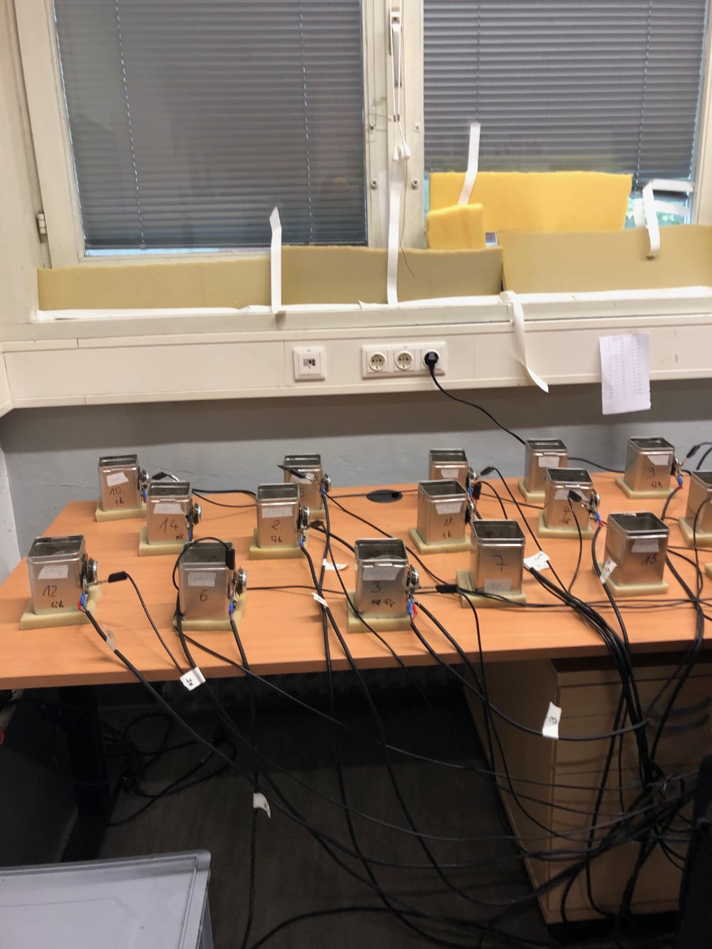 a table in a room (against a window) with numbered metal cans and wires 