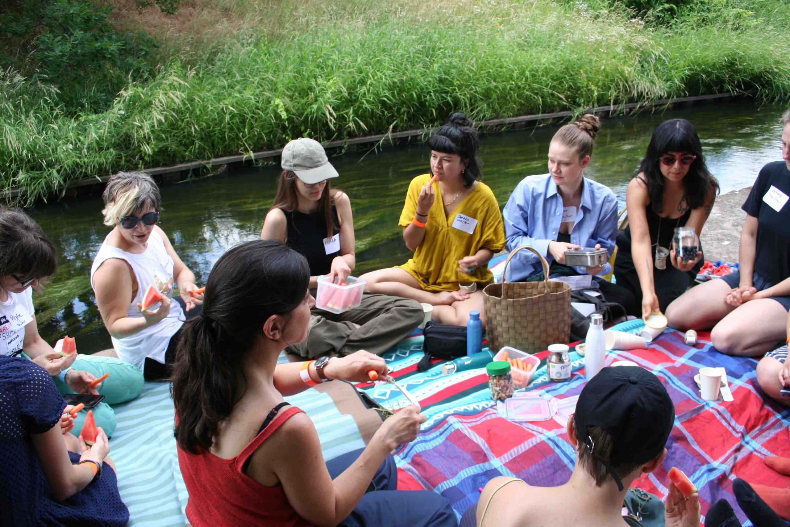 a group of women seated near  a stream , sitting on blankets
