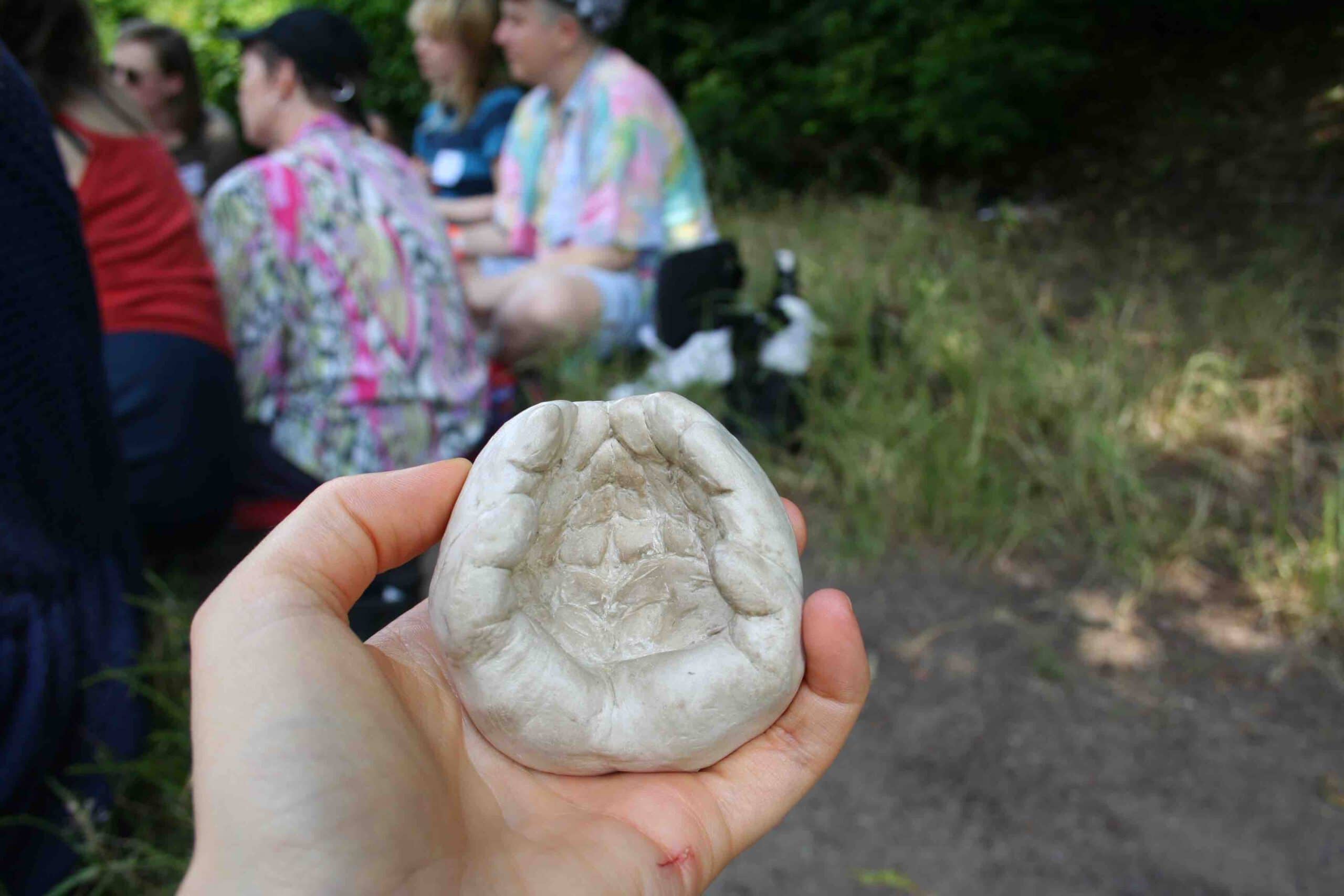 a hand holding a grey clay sculpture