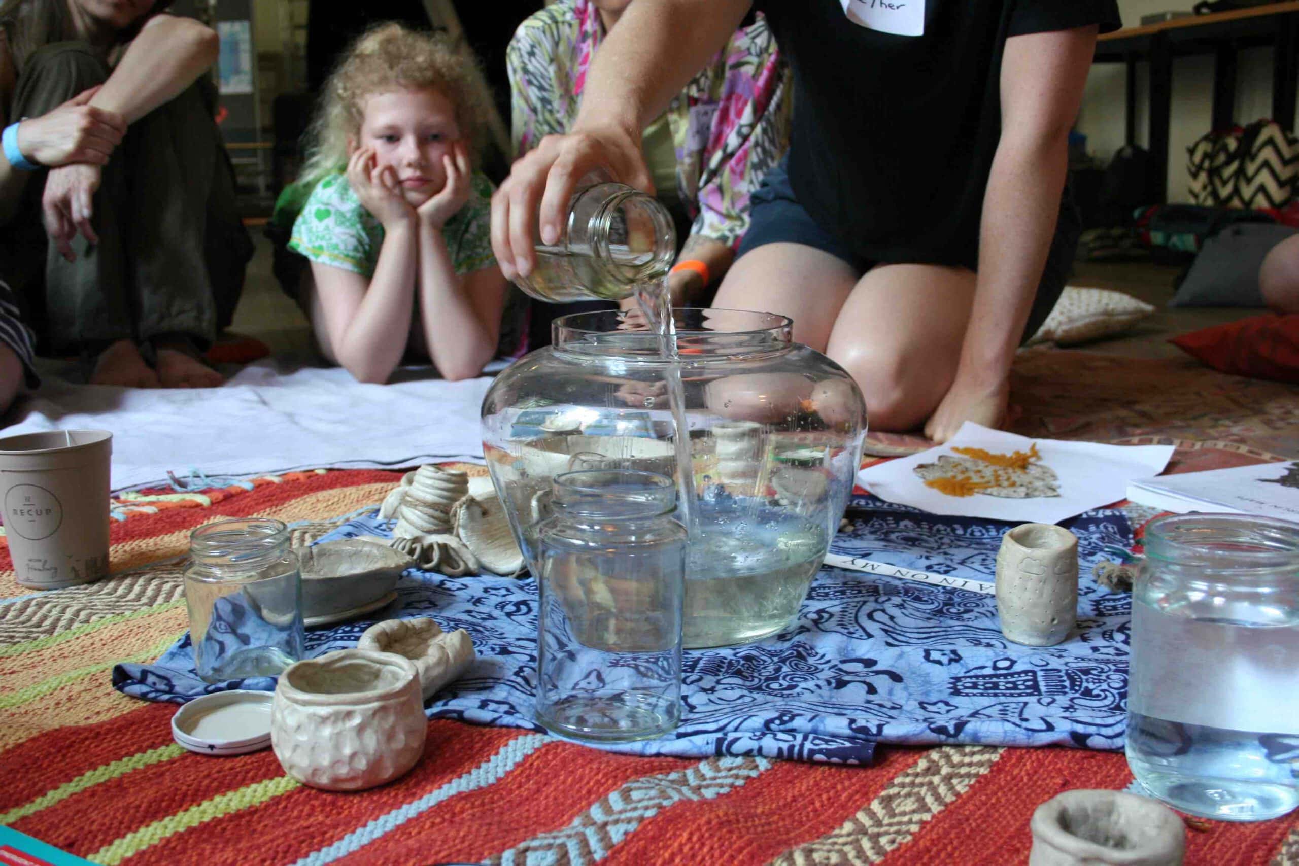 a hand pours a jar of water into a large glass vessel