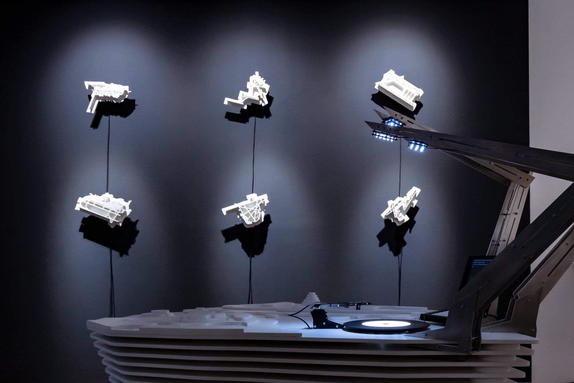 six white architectural models of airports on a grey wall. a table with arm and scanner that looks like a turntable in the foreground
