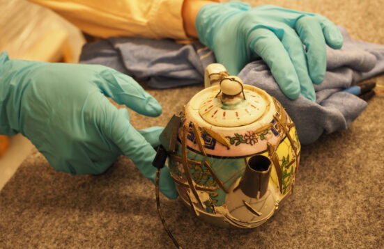 hands with blue gloves steadying a teapot with a sound device attached