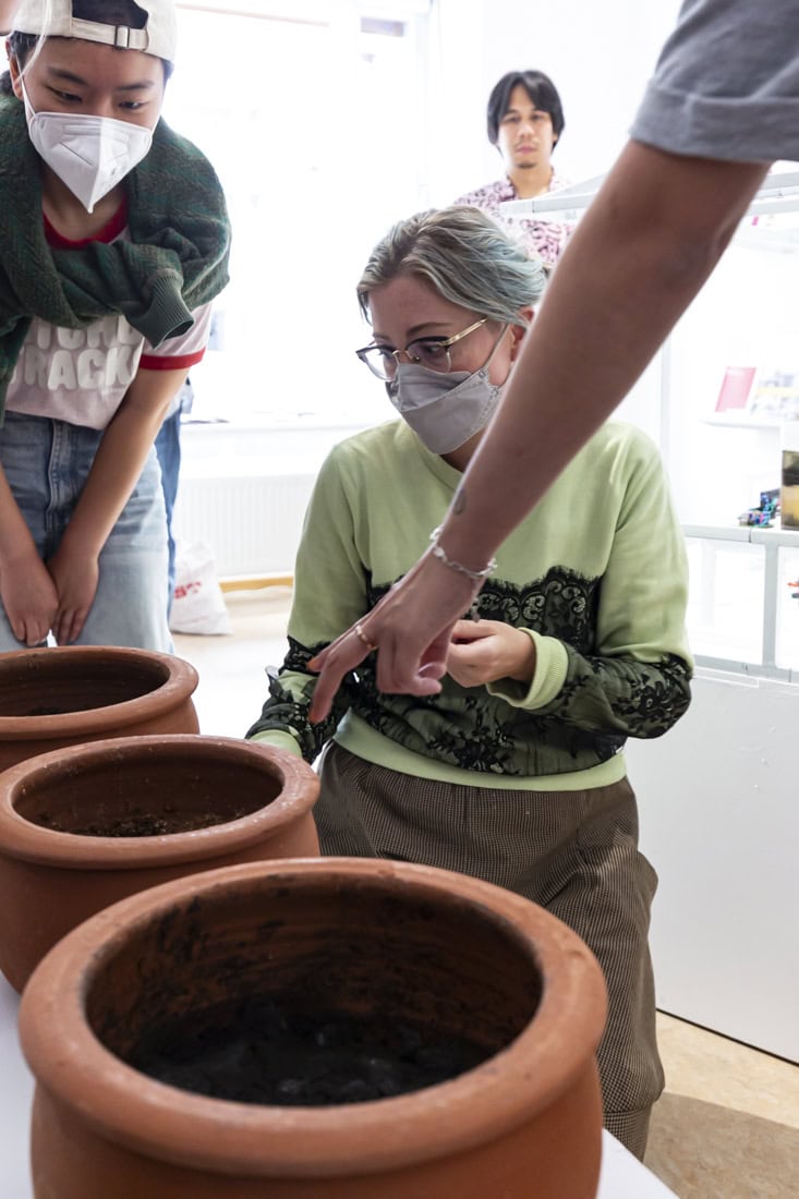 people wearing masks looking at pots of earth