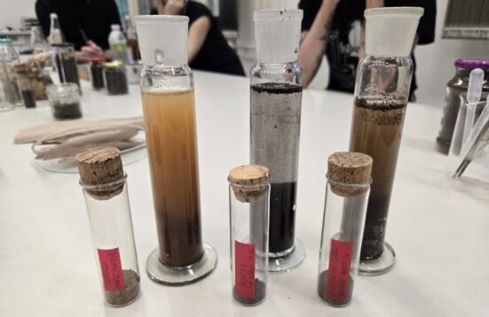 flasks and graduated cylinder son a table people sitting in the background