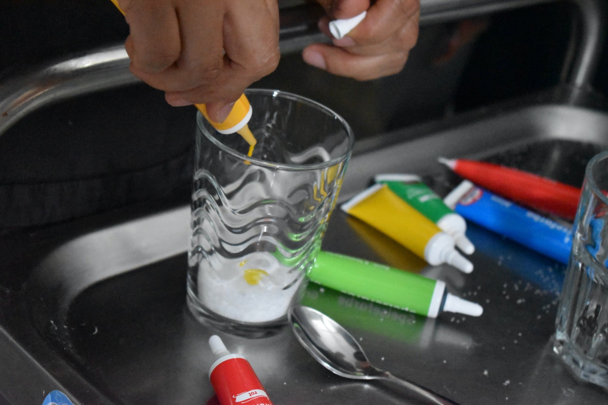 a hand squeezes yellow paint or food coloring into a glass