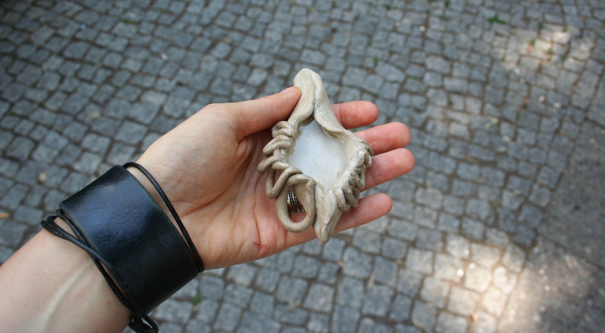 a hand holding a clay sculpture that resembles a vulva