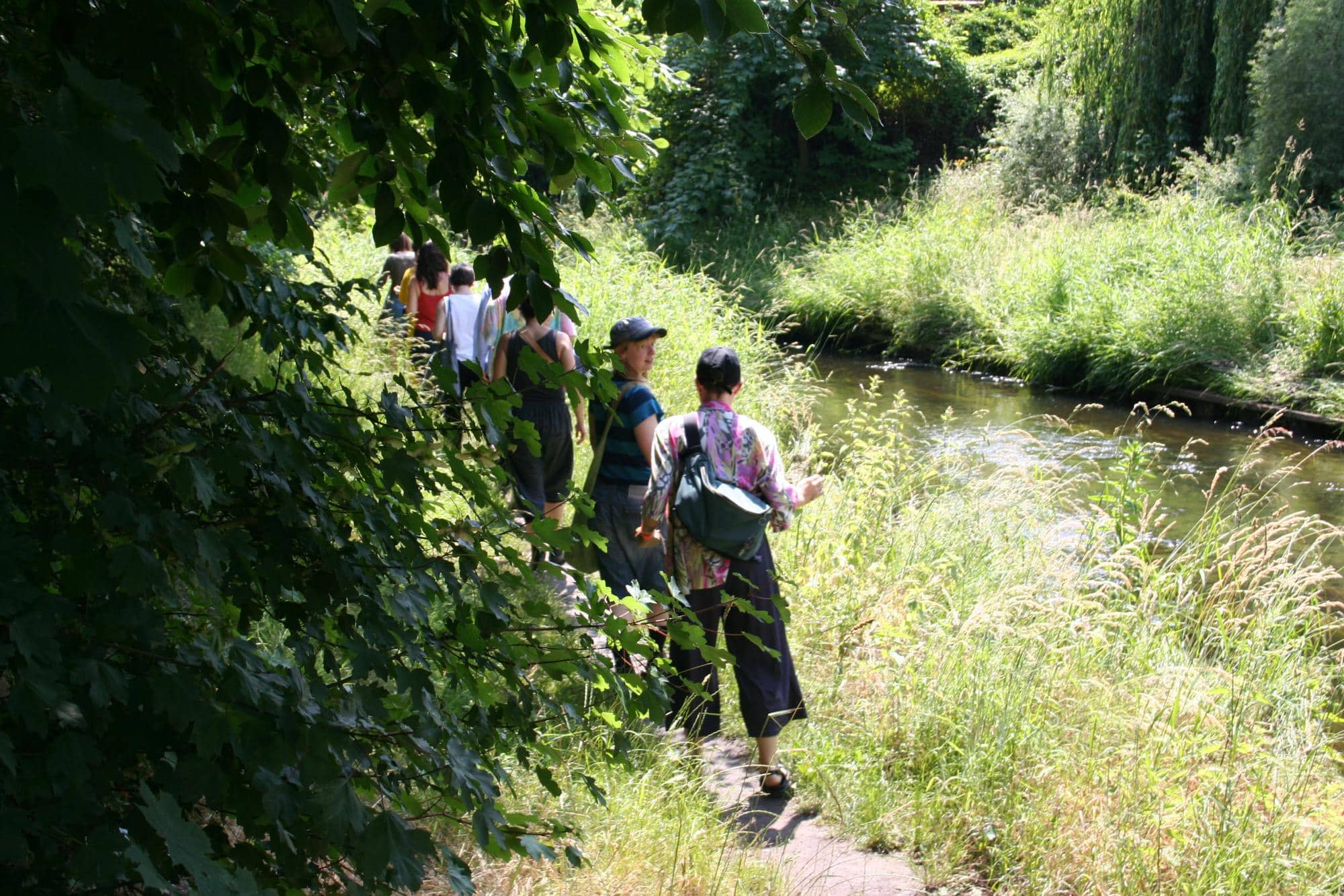 a group of people walking on a path beside a small river