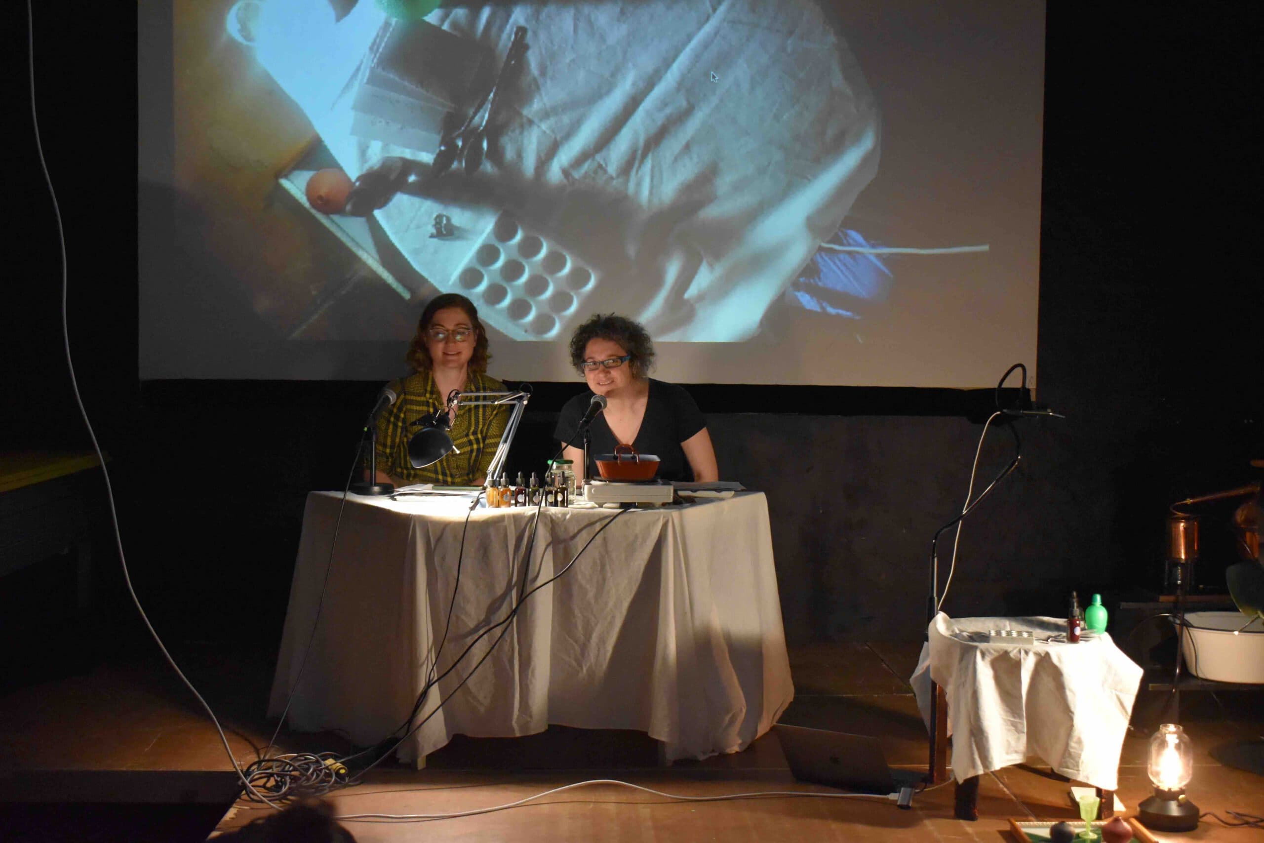 two women seated at a table. a projection in the background