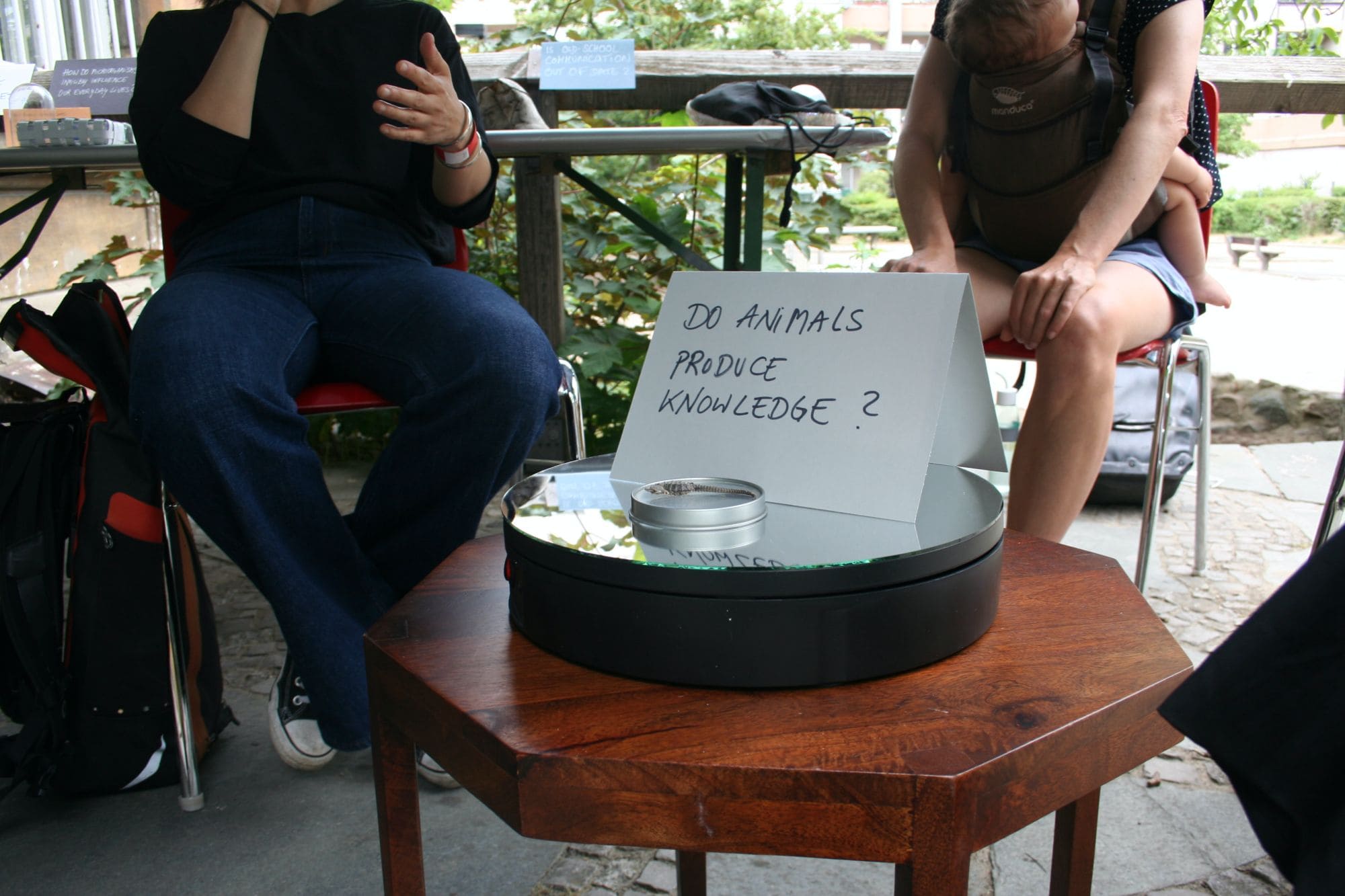 two people seated at a small table a folded paper with the words: "Do Animals Produce Knowledge?"