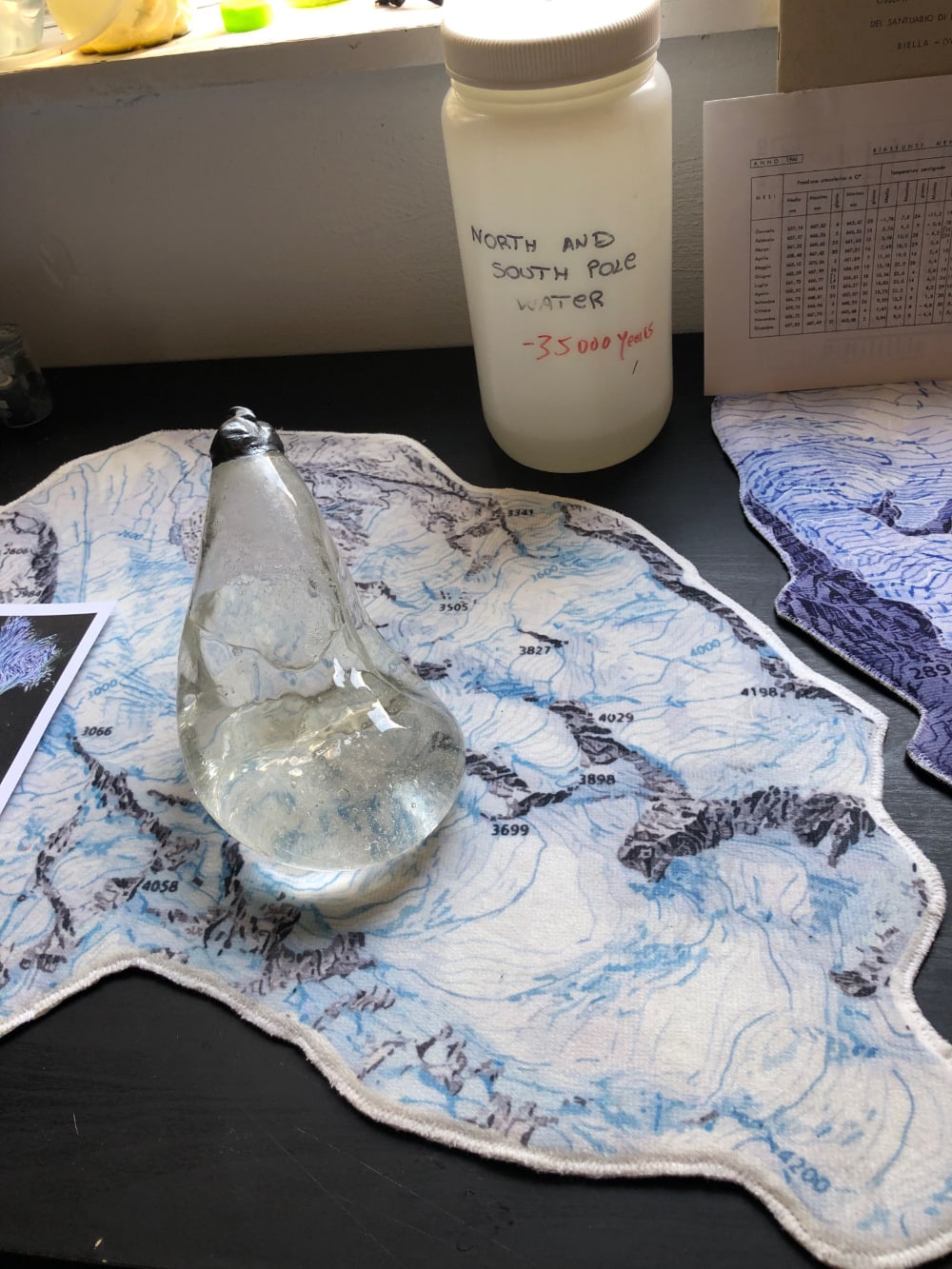 a table with a glass object, a map and a plastic container with the words "North and South Pole water - 35000 years" written on it