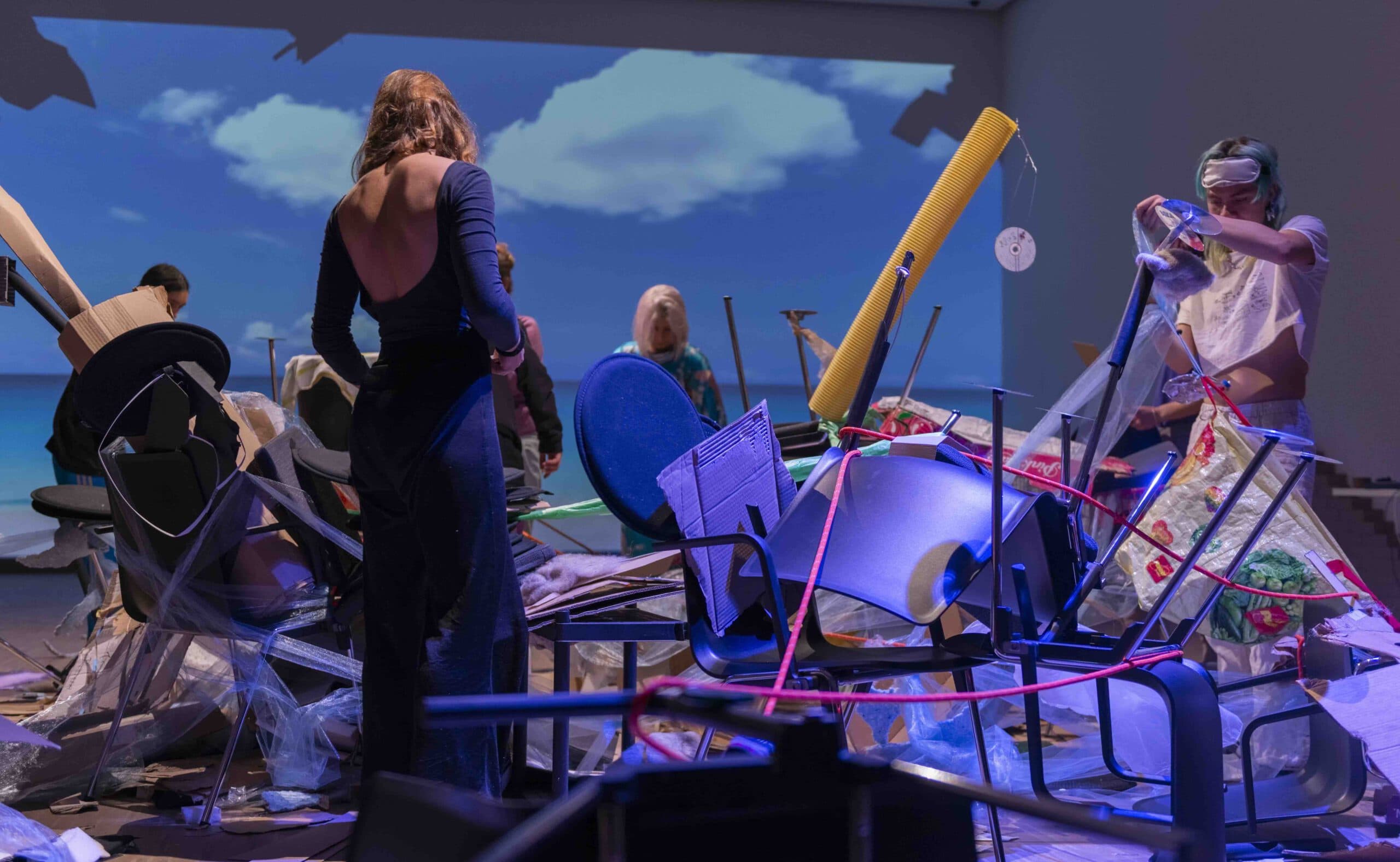 people building an installation of found material. Background: a projection of sea and clouds