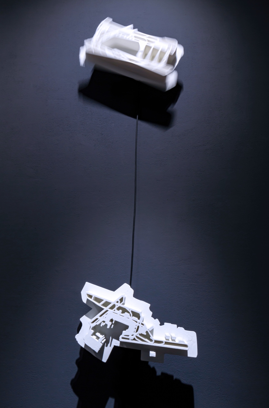 Above a blurry turn of a white architectural model turning on a grey wall. Below a stationary model