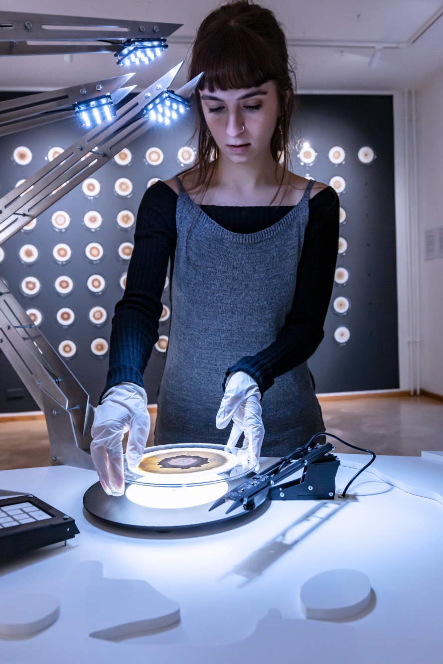 A woman wearing white gloves placing a disc with brown circular forms on a scanner that resembles a turntable