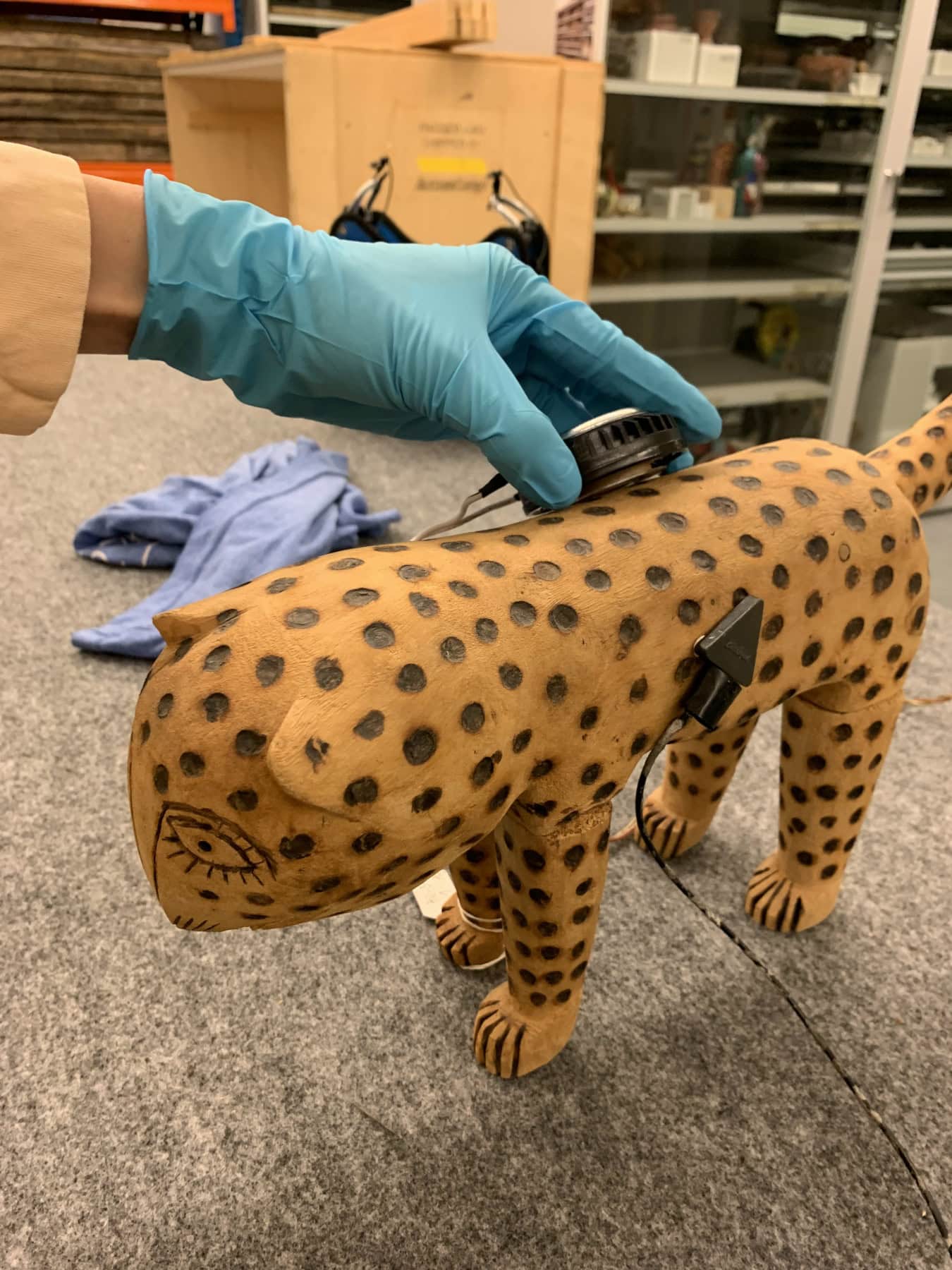 a sculpture of a leopard with a small speaker and microphone attached. A hand with a blue glove in the background