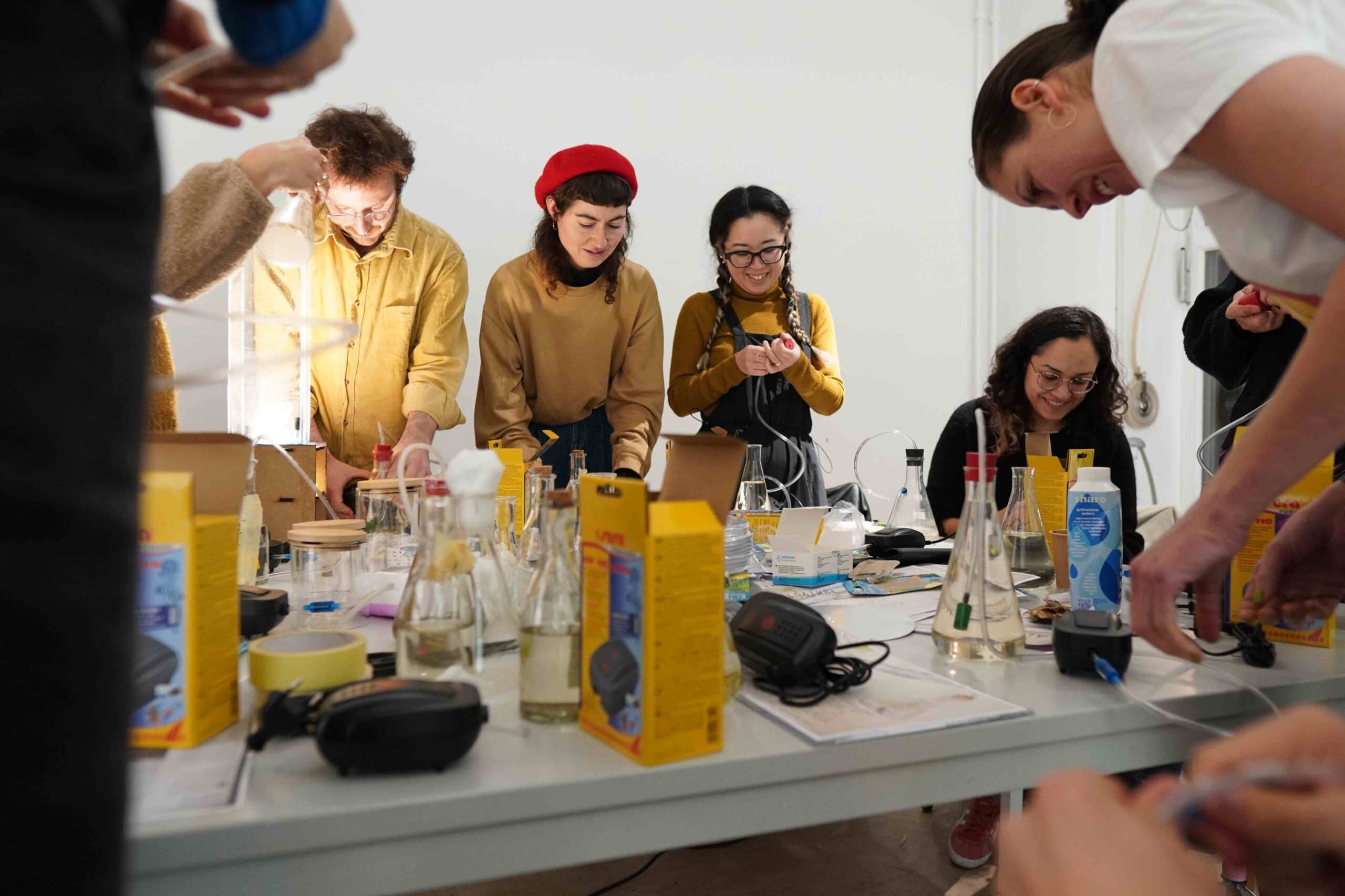 people building something with flasks and tubing and air pumps around a table