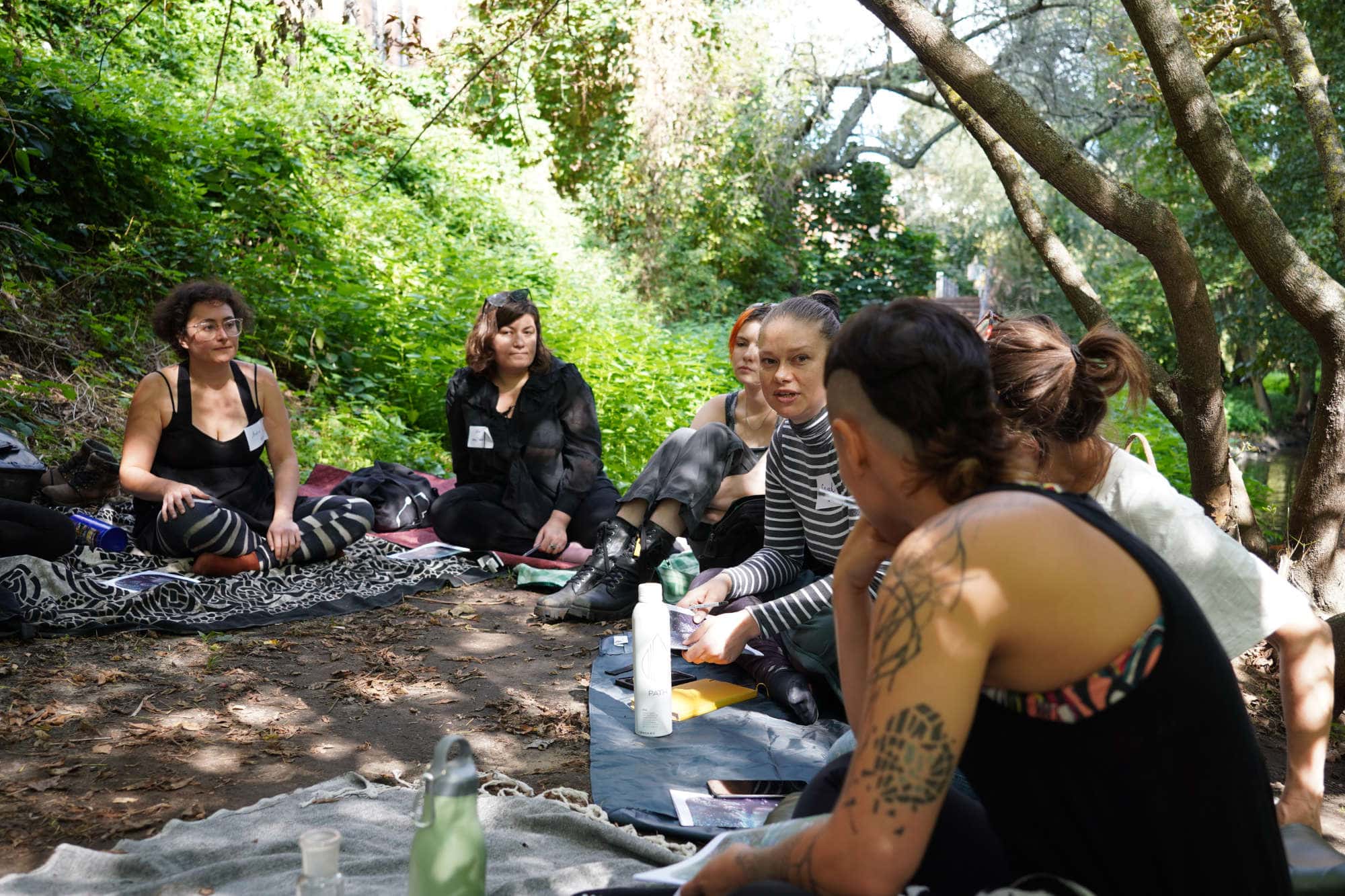 Group of people sitting and talking near a river under trees