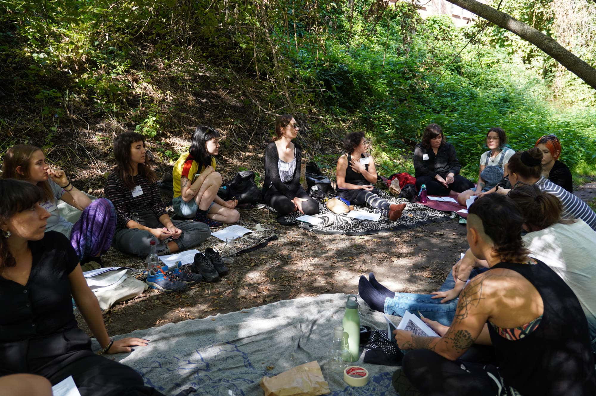 group of people sitting and talking under trees beside a river