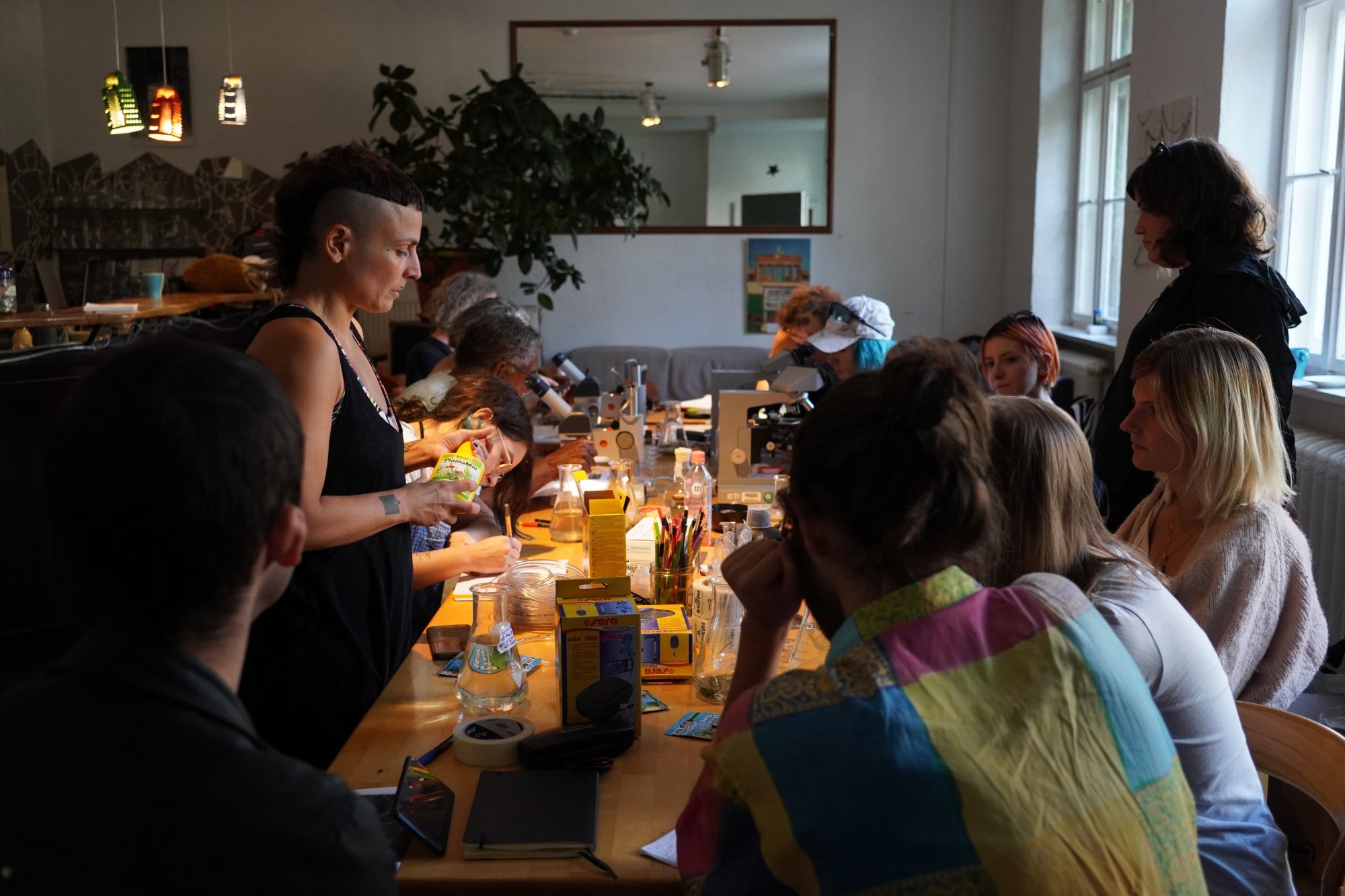 people sitting around a table with flask and microscopes, drawing and talking