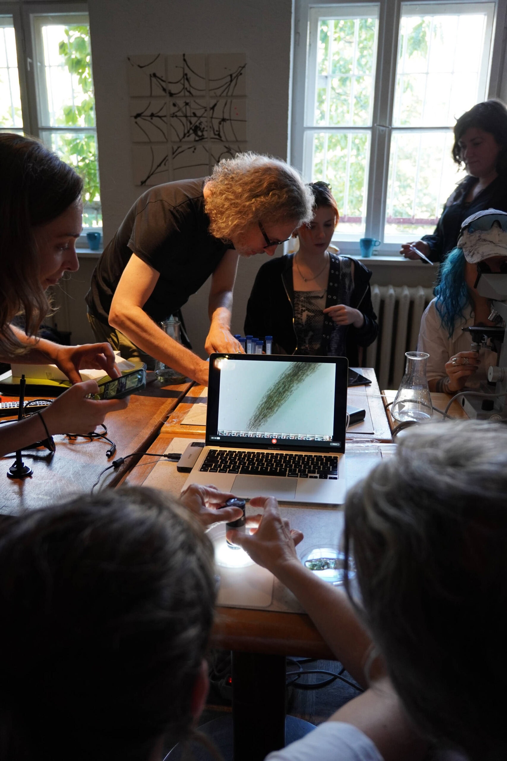 people sitting around a table with flask and microscopes, drawing and talking